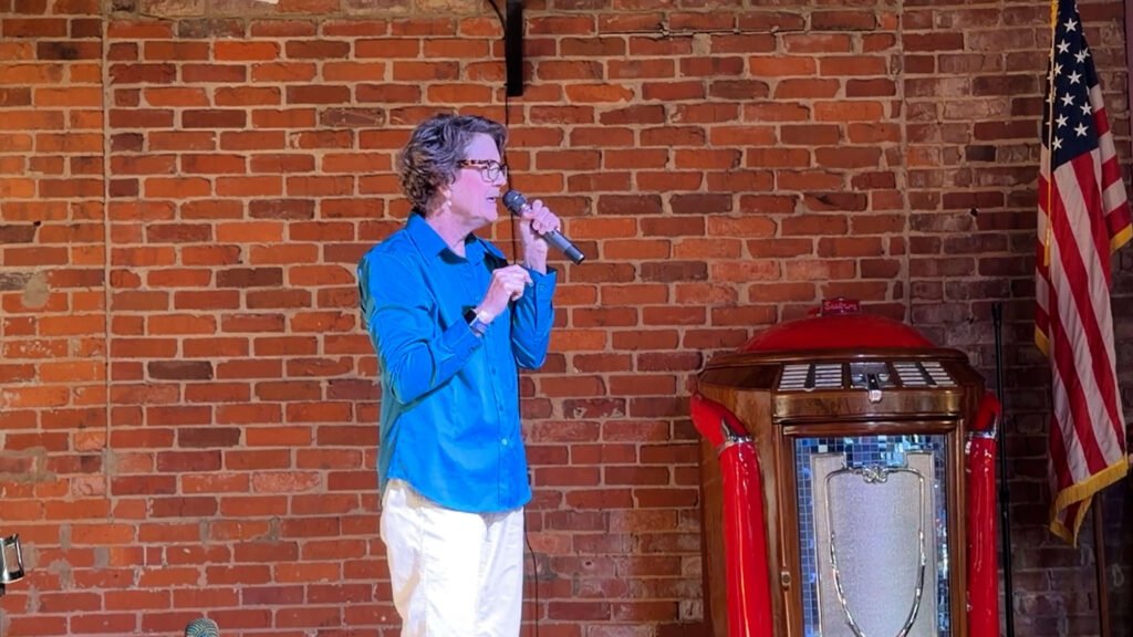 Keynote speaker Sandy Vecchi speaking on stage with a microphone